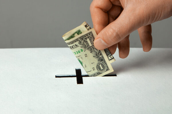 Man puts donation in his hand with dollar in slot in the form of Christian cross
