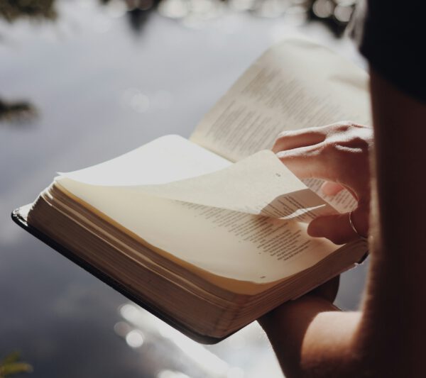 A person is turning the page of a Bible, lit by warm sunlight.